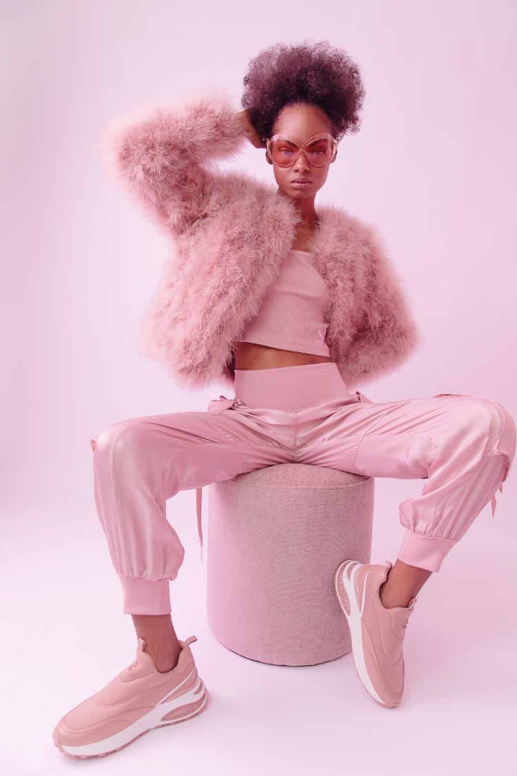 African American model wearing Jimmy Choo sneakers, pink satin cargo pants, and a feathered jacket.