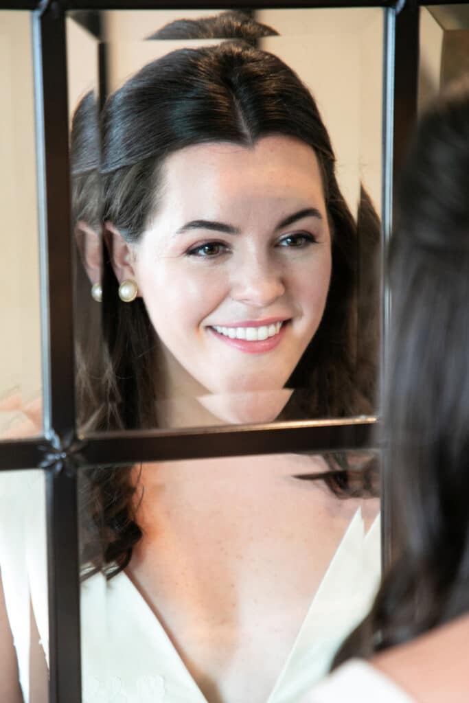 Bride smiling in the mirror after having her makeup done by Chicago makeup artist Traci Fine